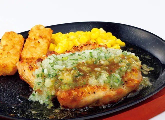 鉄板にのった焼いた鶏肉に刻みたまねぎのソースをかけ、ポテトとコーンを添えた若鶏のディアボラ風