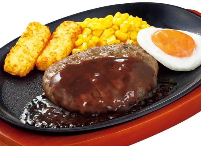 鉄板にのったソースがけのハンバーグに、目玉焼き・ポテト・コーンを添えたハンバーグステーキ